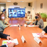 Varias personas reunidas en torno a una mesa con un sistema de videoconferencia